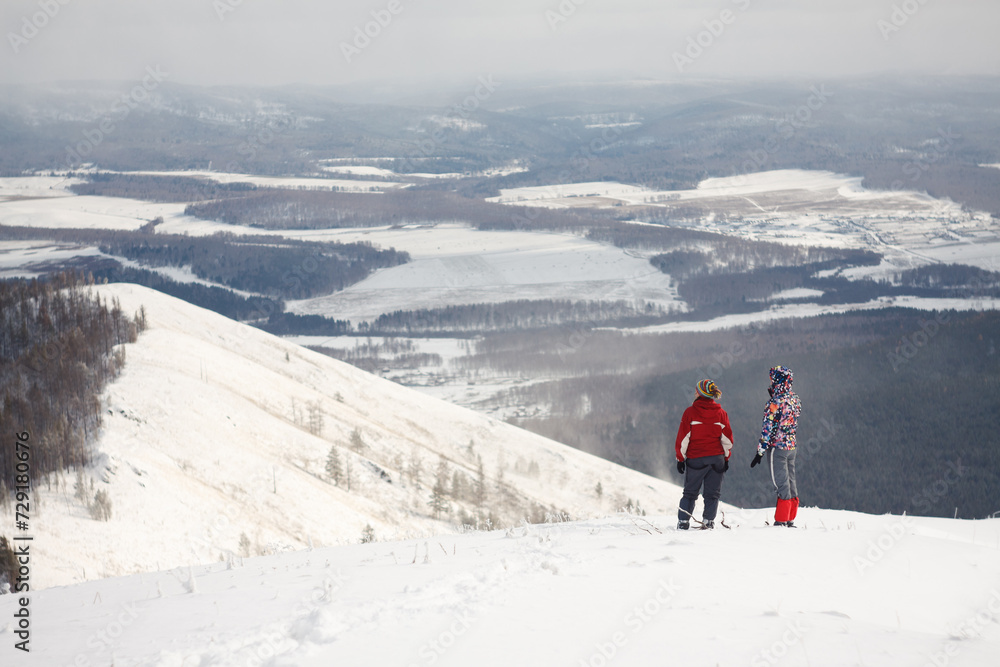 Two snowboarders admiring scenic winter landscape on snowy mountaintop with blue sky and white snow