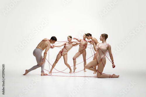 Elegant female ballet dancers pulling man with red strings symbolizing affection and control against white studio background. Concept of classical dance, modern style, inspiration, psychology