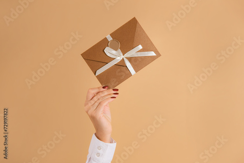 female hand hold discount card or gift certificate in envelope on studio beige background