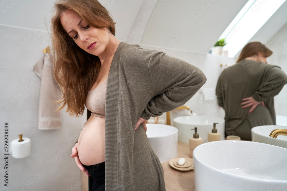 Caucasian woman feeling backache while standing in the bathroom Caucasian woman feeling backache while standing in the bathroom