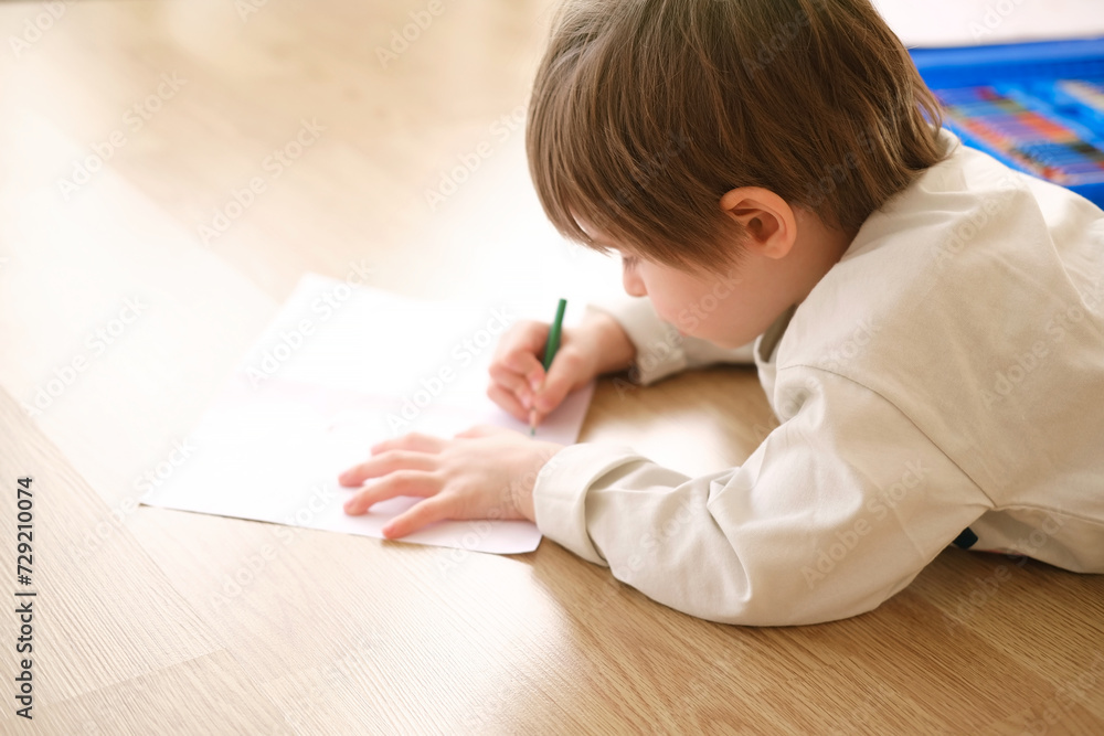 Creative child drawing with colored pencils on big white sheet, view from side Creative child drawing with colored pencils on big white sheet, view from side