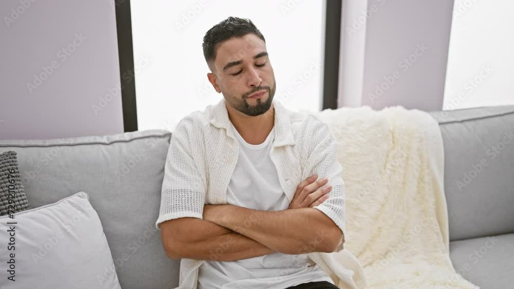 Handsome young arab man skeptically crosses arms, personifying a wave of nervous negativity at home, sitting on sofa Handsome young arab man skeptically crosses arms, personifying a wave of nervous negativity at home, sitting on sofa