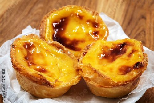 Pastel de nata tarts or Portuguese egg tart on a wooden brown background. Pastel de Belem is a small pie with a crispy puff pastry crust and a custard cream filling. Sweet dessert. photo