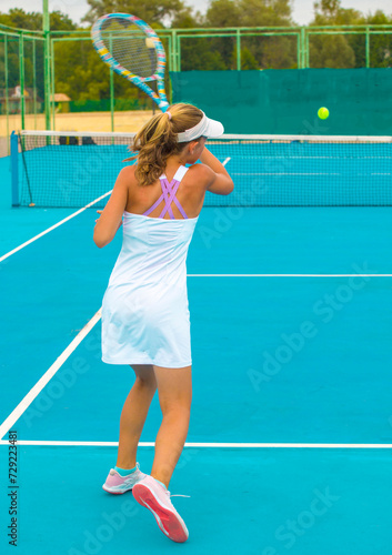 A girl plays tennis on a court with a hard blue surface on a summer sunny day  © Павел Мещеряков