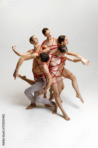 Talented artistic young people, man and women, ballet dancers performing, tied with red string, dancing against white studio background. Concept of classical dance, modern style, inspiration