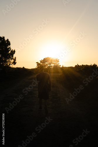 Back view of a hiker with a backpack walking along the trail at sunset on a summer afternoon