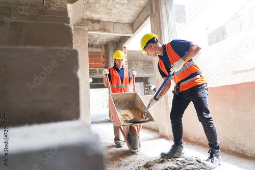 Young male and female masons working together while mixing cement at incomplete housing development photo