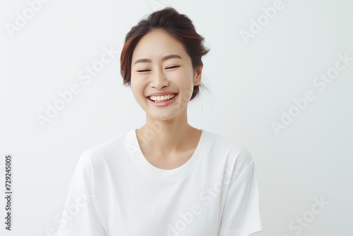 Young Asian woman in serene smile, wearing white relax pajamas against a plain white background. Generative AI. © Surachetsh