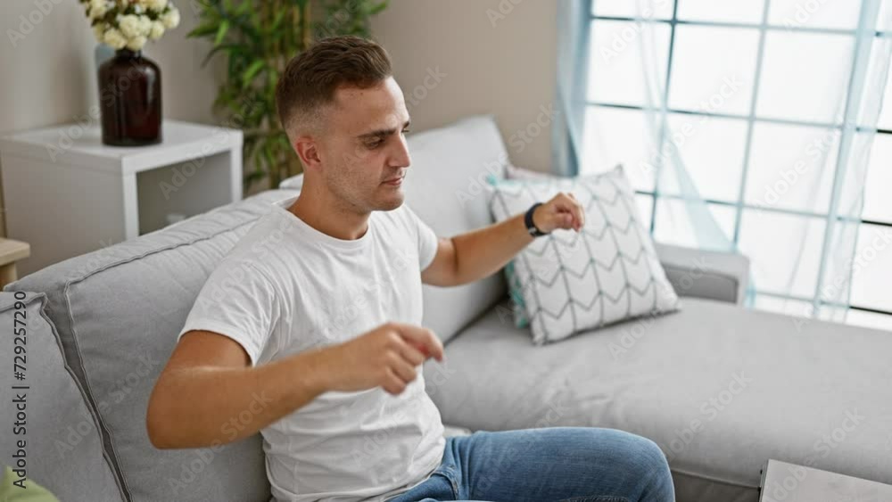 A young hispanic man in casual attire relaxes on a modern sofa in a well-lit living room, portraying a sense of calm domesticity. A young hispanic man in casual attire relaxes on a modern sofa in a well-lit living room, portraying a sense of calm domesticity.
