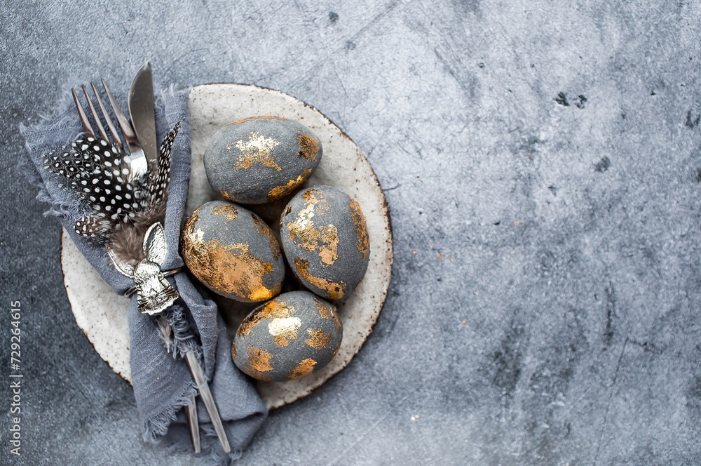 able setting. A fashionable concrete plate with a rabbit on a napkin, Easter eggs with gilding, feathers on a gray background. The concept of a Happy Easter holiday for cafes and restaurants. able setting. A fashionable concrete plate with a rabbit on a napkin, Easter eggs with gilding, feathers on a gray background. The concept of a Happy Easter holiday for cafes and restaurants.