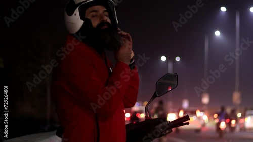 Beard men of Indian ethnicity parking electric scooter near roadside at night and talking on mobile phone portrait close up photo