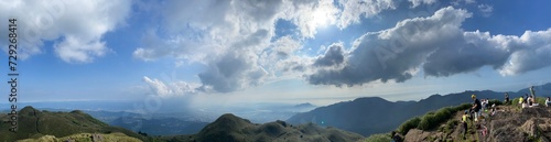 A panoramic view of overlapping mountain ranges, with sunlight piercing through the clouds in the sky, while the mountains are shrouded in mist.