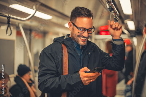 A cheerful adult businessman typing text messages on his phone while taking a train ride