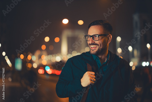 A cheerful adult businessman walking back home during night and admiring the city photo