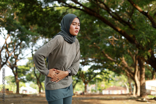 Asian veiled muslim woman having pain on right stomach while doing outdoor exercise in the morning