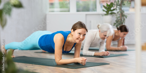Nice girl with other sporty people relaxing and enjoying yoga in fitness center