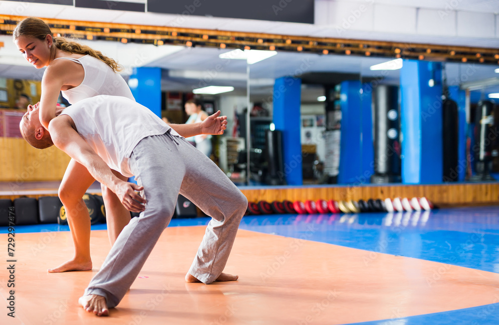 Concentrated young female practicing effective self defence techniques with coach in training room