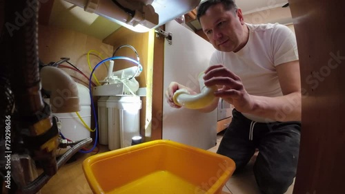 A man disassembles the plumbing under the sink for cleaning and maintenance. He connects the V-pipe after service photo