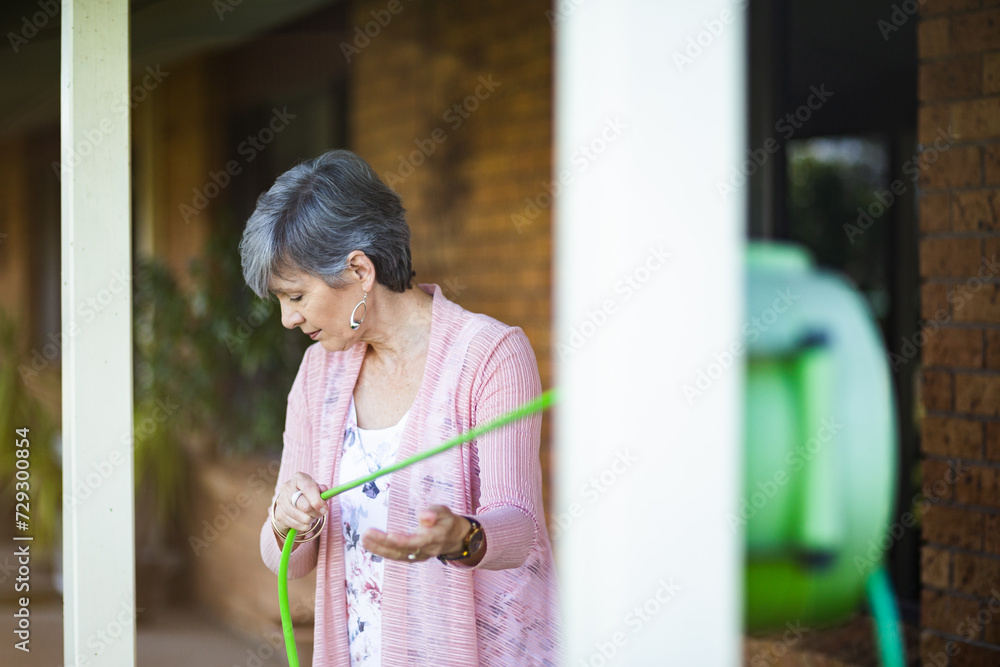 senior woman unrolling garden hose to water her flowers senior woman unrolling garden hose to water her flowers