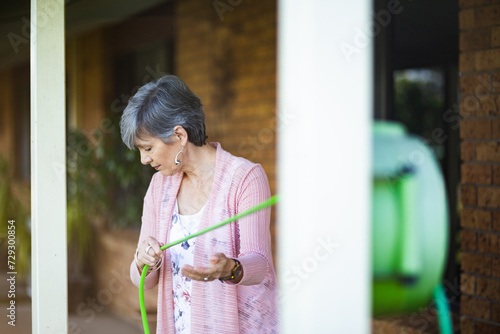 senior woman unrolling garden hose to water her flowers photo