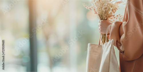 Woman's hand holding eco shopper bag and flowers. Banner with copy space. Ecology, reasonable consumption, sustainable lifestyle choices concept photo