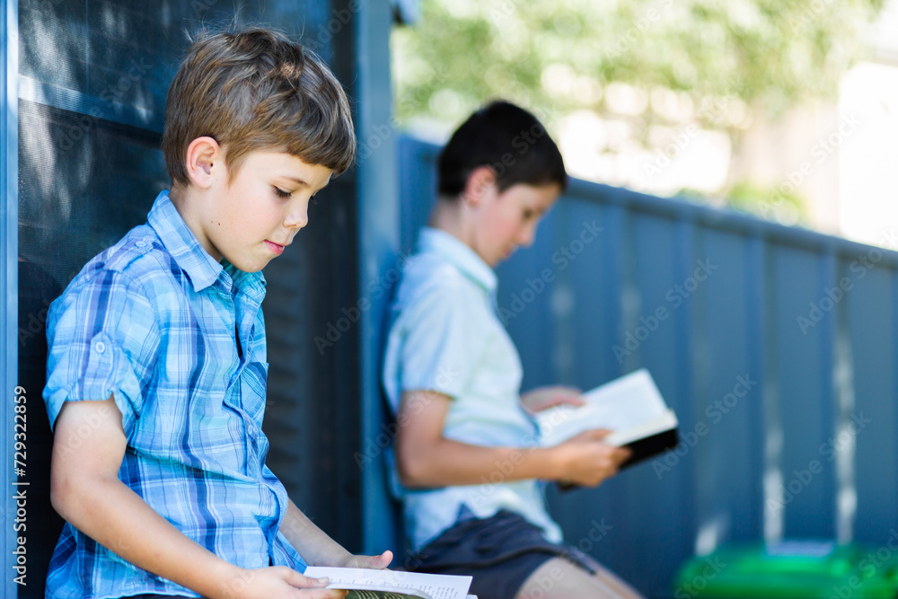 Brothers sitting against window in backyard reading books