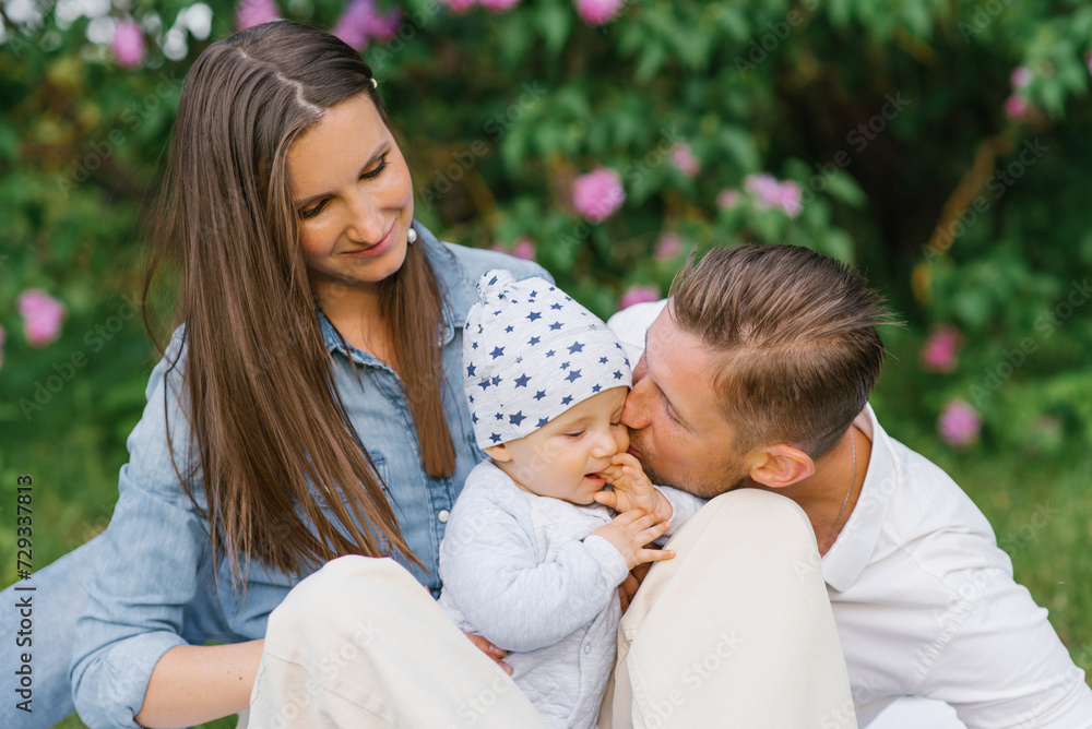Happy Caucasian family with a young son relax in the park in spring or summer, sitting on a blanket. Dad kisses the boy on the cheek Happy Caucasian family with a young son relax in the park in spring or summer, sitting on a blanket. Dad kisses the boy on the cheek