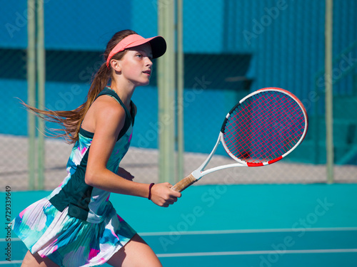 A girl plays tennis on a court with a hard blue surface on a summer sunny da