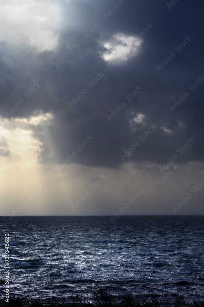 Storm at sea with the sun shining through dark clouds, lighting up the waves