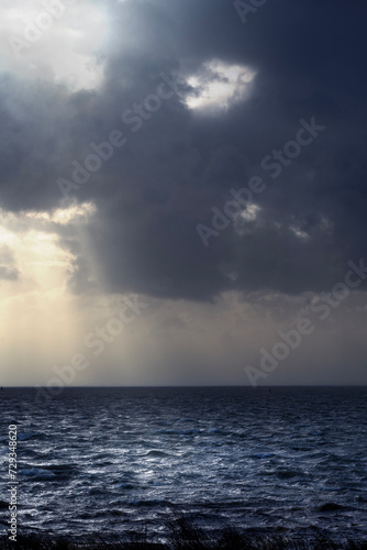 Storm at sea with the sun shining through dark clouds, lighting up the waves