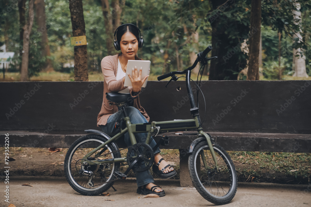 Happy young Asian woman while riding a bicycle in a city park. She smiled using the bicycle of transportation. Environmentally friendly concept.