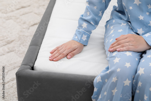 Woman sitting on new soft mattress indoors, closeup