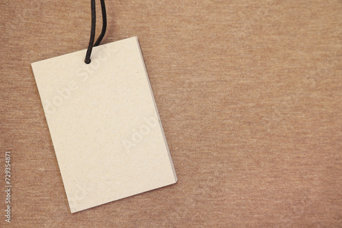 Cardboard tag on brown garment, top view. Space for text