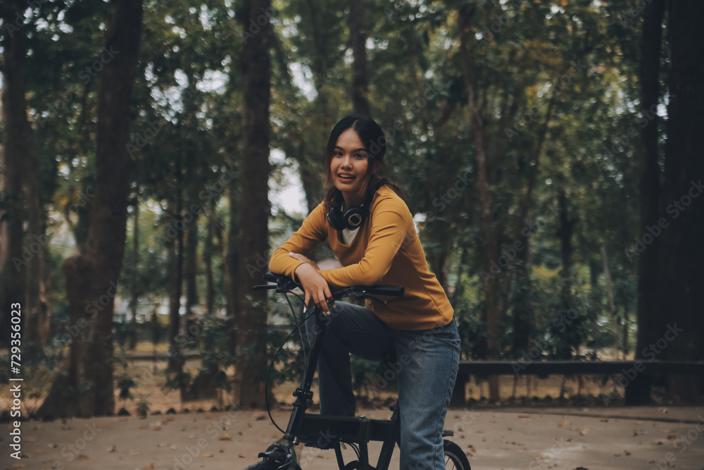 Happy young Asian woman while riding a bicycle in a city park. She smiled using the bicycle of transportation. Environmentally friendly concept. Happy young Asian woman while riding a bicycle in a city park. She smiled using the bicycle of transportation. Environmentally friendly concept.