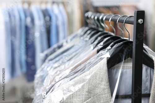 Dry-cleaning service. Many different clothes in plastic bags hanging on rack indoors, closeup photo