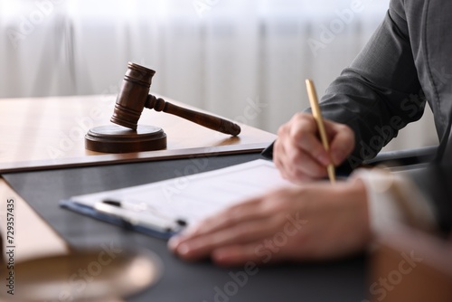Notary writing notes at wooden table in office, closeup