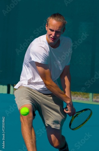 Tennis player playing tennis on a hard court on a bright sunny day	