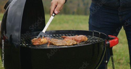 Close up shot of tourist puts meat on grill. Man cook tasty dinner on BBQ grill outdoor. Family stopped to rest after long expedition at mountains. Nature discovery and active recreation. Slow motion.