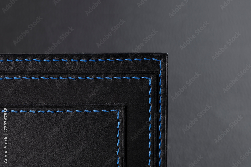 Black leather wallet with blue stitching on a black background.