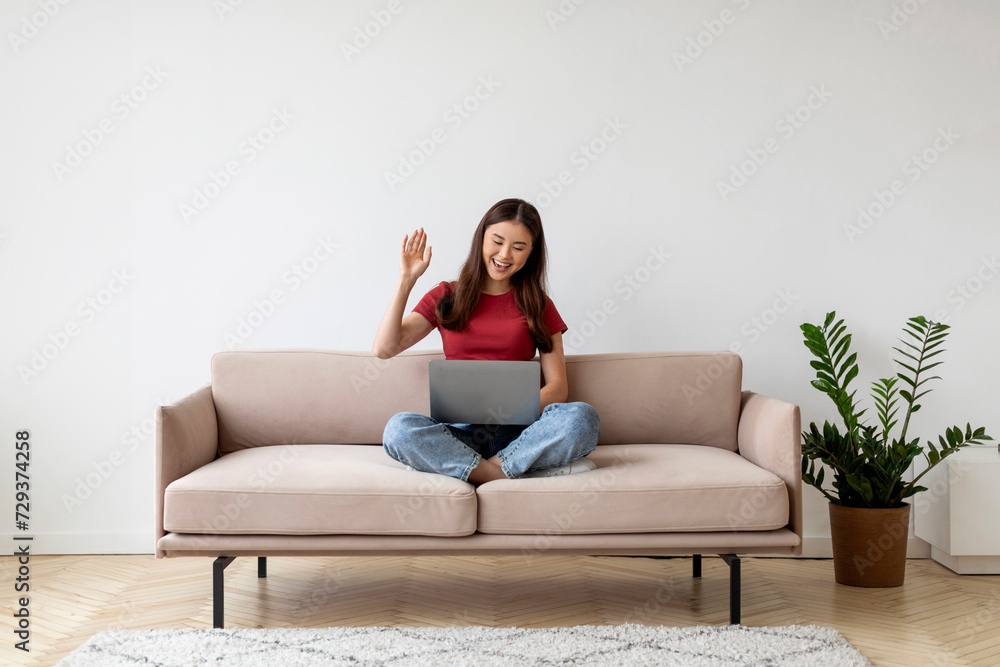 Cheerful asian woman using laptop for video call, sitting cross-legged on sofa Cheerful asian woman using laptop for video call, sitting cross-legged on sofa