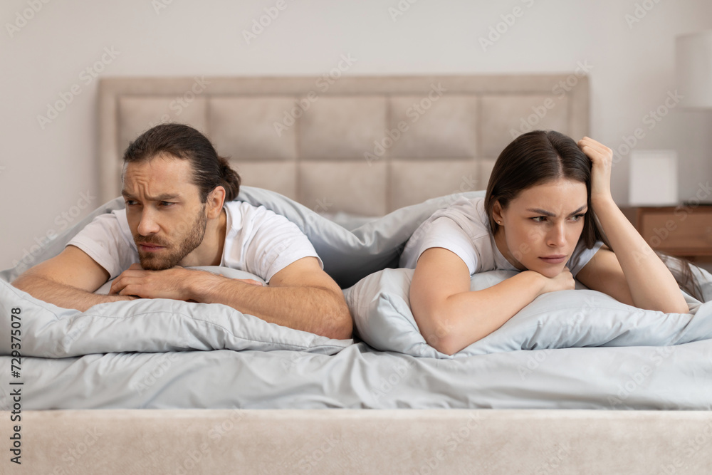 Couple in bed with worried expressions facing away Couple in bed with worried expressions facing away