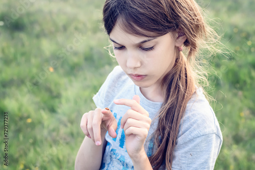 Little girl on the background of a green field looking at a ladybug on her finger
