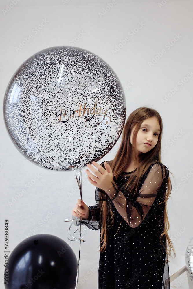 Naklejka premium A little girl celebrates her 10th birthday. A girl on a white background in a black dress with long straight hair. Party, holiday