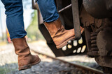 Action of a man wearing leather safety shoe is climbing up on the train locomotive driver cabin ladder. Transportation industrial working action scene. Close-up and selective focus.
