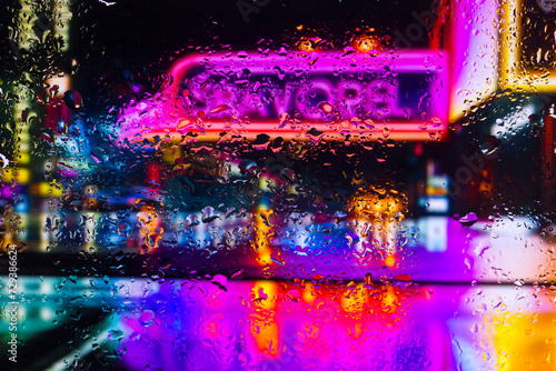 View through a glass window with raindrops on city streets with cars in the rain, bokeh of colorful city lights, night street scene. Focus on raindrops on glass  © Павел Мещеряков