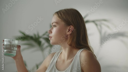 Pensive young woman taking sip of water. Attractive thirsty girl drinking water at home. Healthy habit, stay hydrated photo
