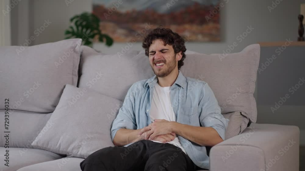 Young caucasian man lying on sofa feeling sudden strong abdominal stomach ache, gastritis problem. White guy having symptom poisoning diarrhea indigestion peptic ulcer pancreatitis at home apartment r Young caucasian man lying on sofa feeling sudden strong abdominal stomach ache, gastritis problem. White guy having symptom poisoning diarrhea indigestion peptic ulcer pancreatitis at home apartment r