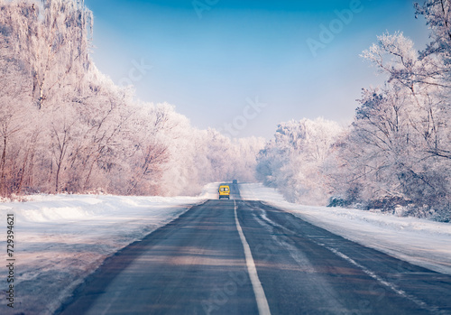 Yellow van on the asphalt road. Fantastic winter view of frosty trees on both sides of the road. Cold morning scene of distant way. Traveling concept background. Beautiful winter scenery.. © Andrew Mayovskyy