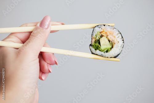 Sushi background. Woman hand holding chopsticks. Futomaki sushi roll. Japanese food isolated on gray wall. Eating sushi with avocado and salmon. Asian food background. Blank copy space wall.