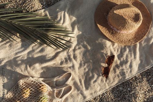 Straw hat, sunglasses, towel, bag on beach sand background. Aesthetic lifestyle, summer vacation concept. Sunbathing, beach party, picnic on summer holiday. Travel fashionable blog, social media.